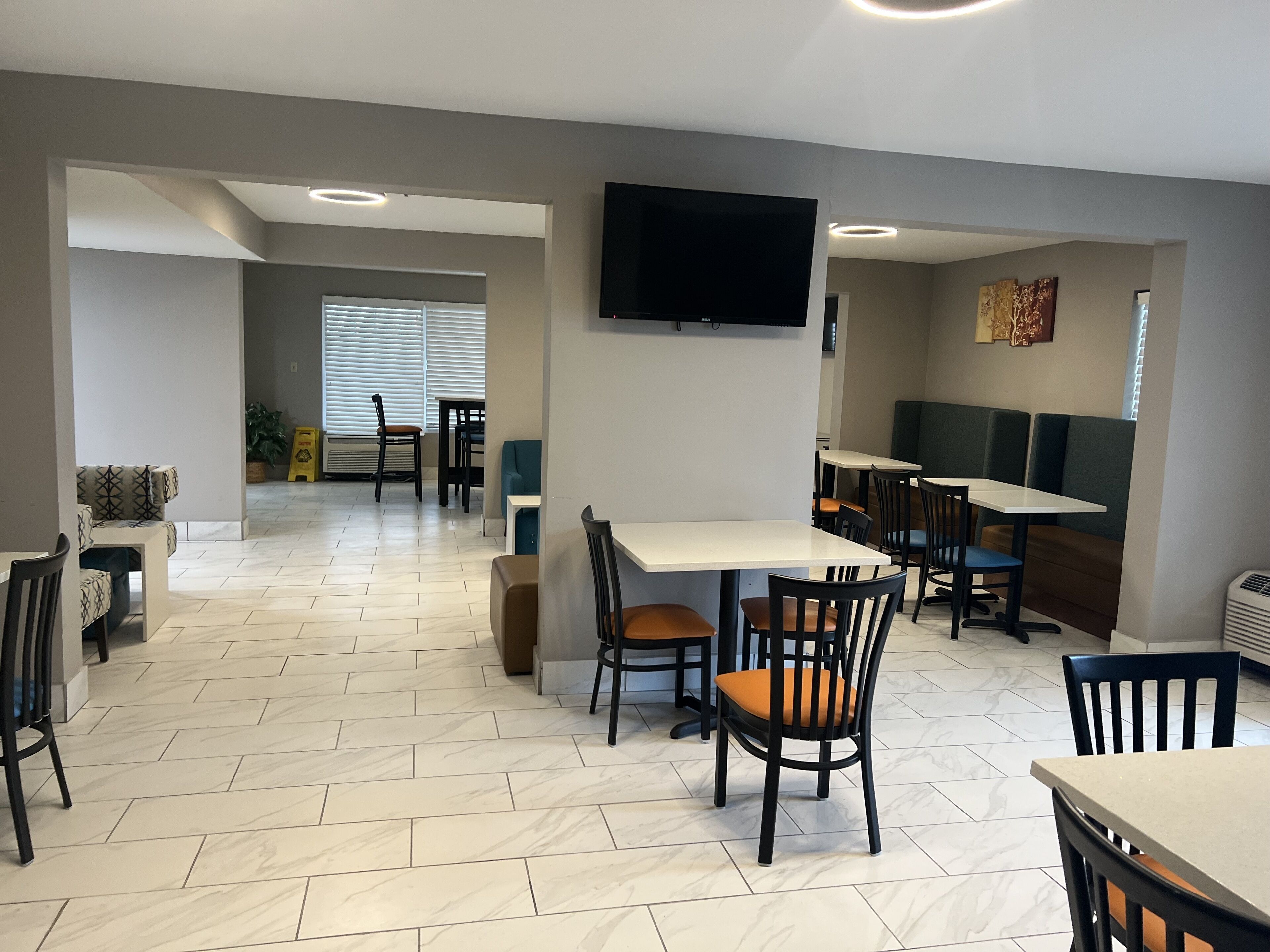 A modern restaurant with herringbone-patterned flooring, multiple tables and chairs, and a flat-screen TV mounted on the wall.