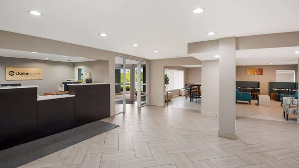 A hotel reception area with a reception desk, a seating area with chairs and tables, and a view of the outdoors through glass doors. - Clarion Pointe Indianapolis Northeast (Indianapolis)