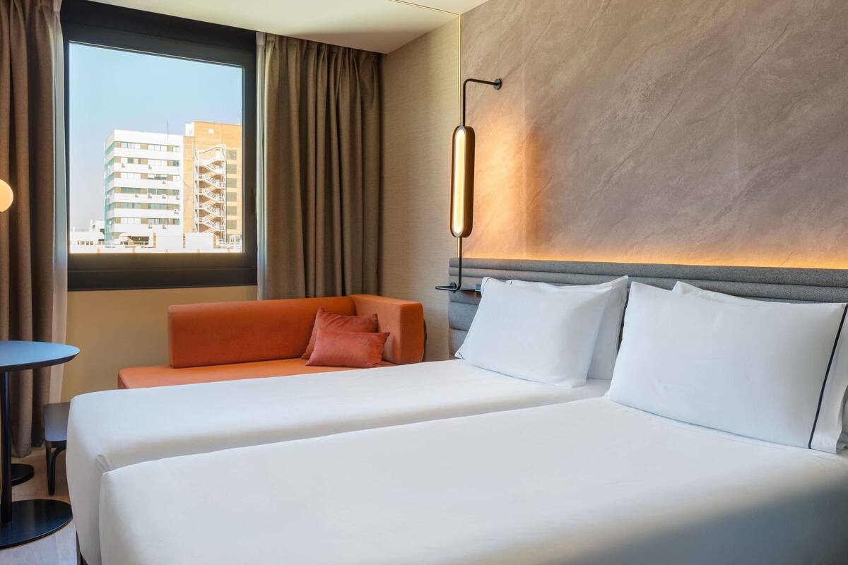 Une chambre d’hôtel avec un grand lit, un canapé, une petite table et une vue sur les bâtiments à travers la fenêtre.