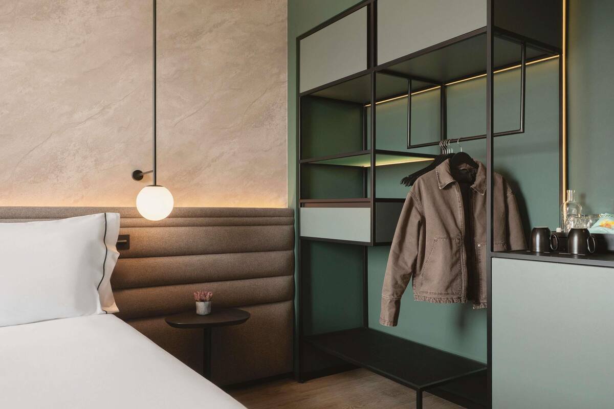 Une chambre d’hôtel moderne équipée d’un lit, d’une table de chevet, d’étagères murales et d’un porte-manteau.