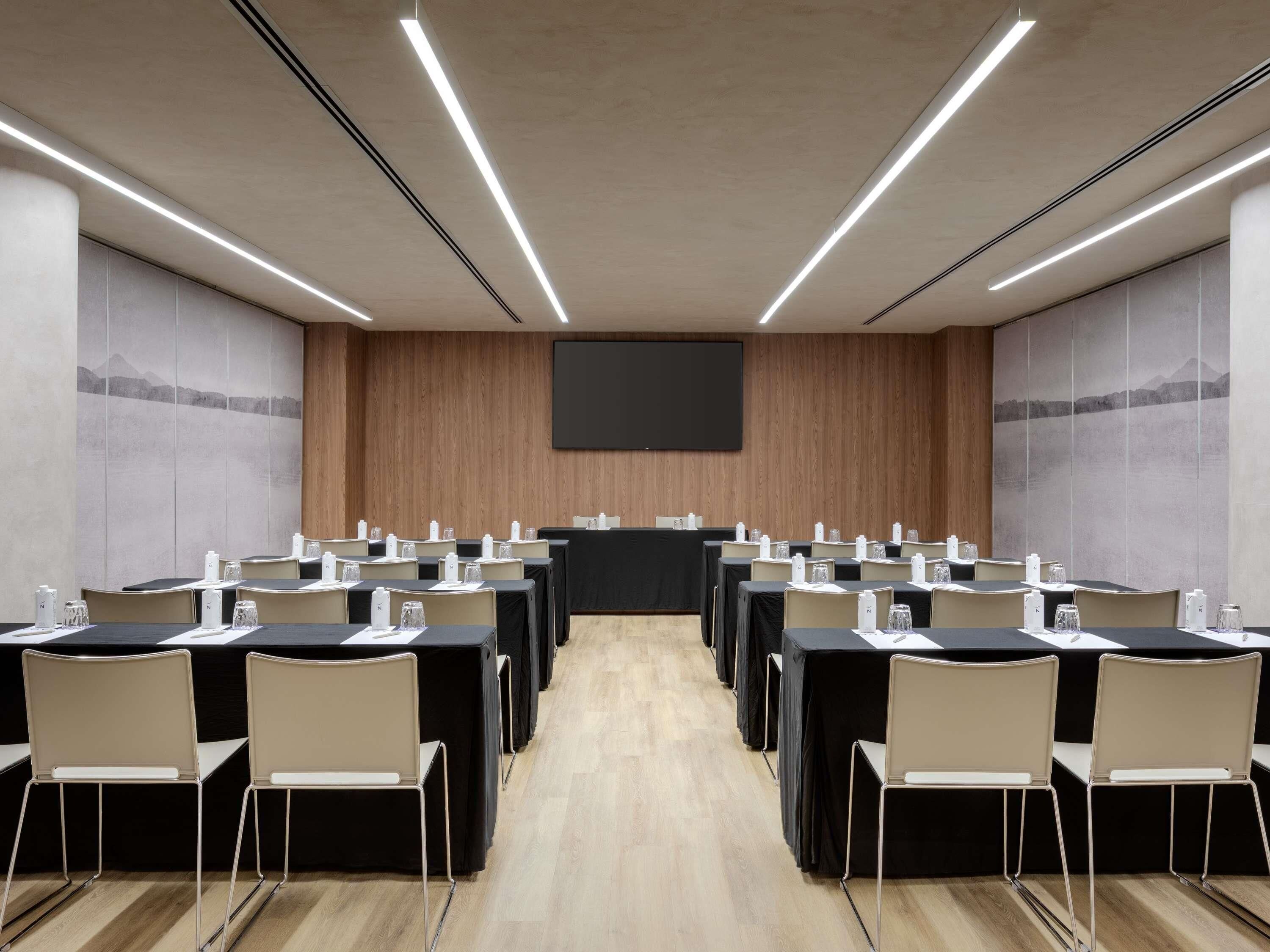 Un salón de conferencias con mesas, sillas, una pantalla de proyector y una pared de madera.