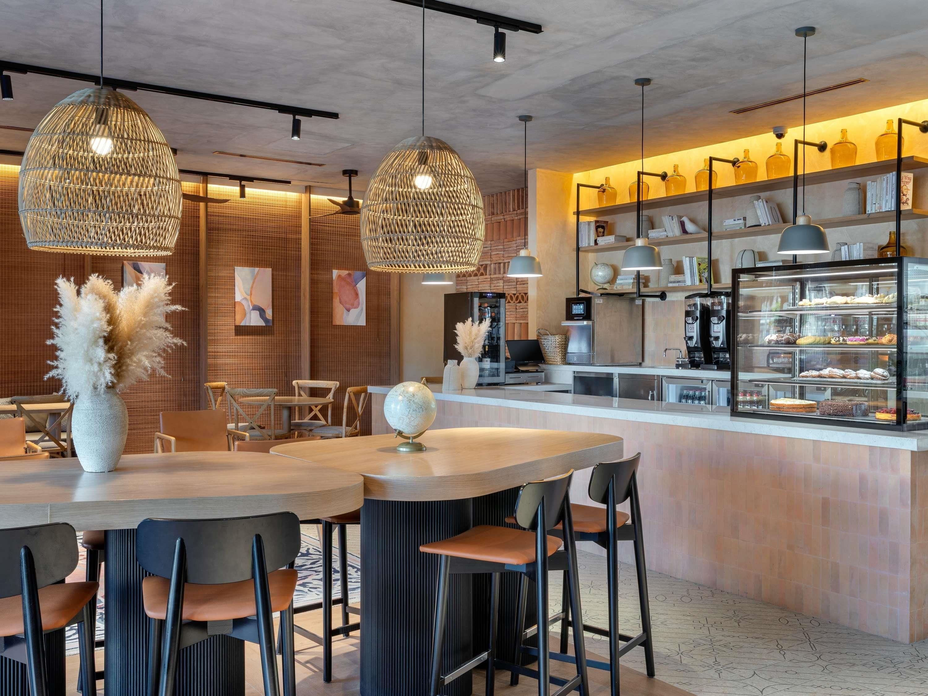 Um café moderno com balcão de madeira, luminárias de vime suspensas e uma vitrine com doces.