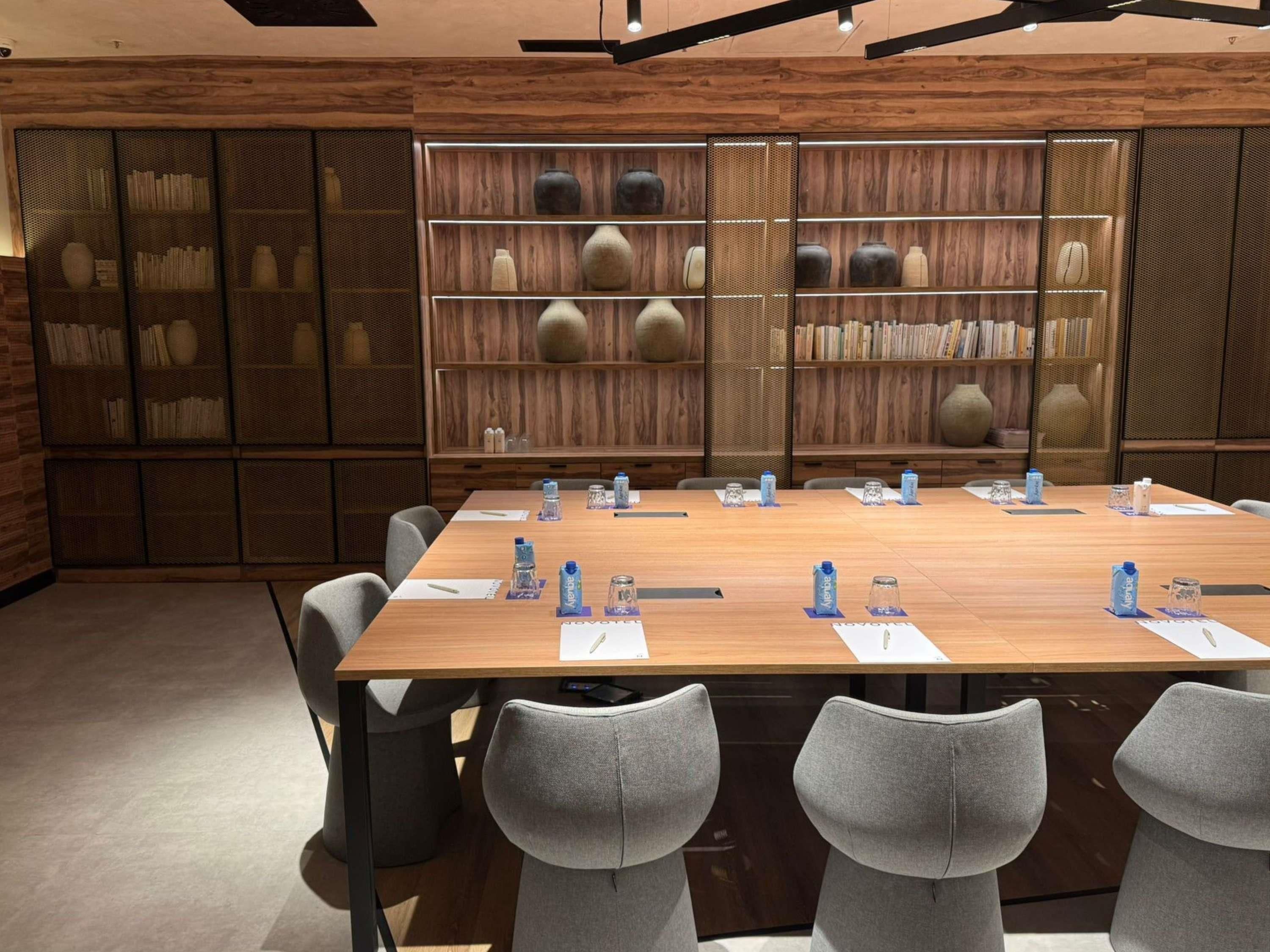 Una sala de conferencias con una larga mesa, sillas grises y estantes con adornos.