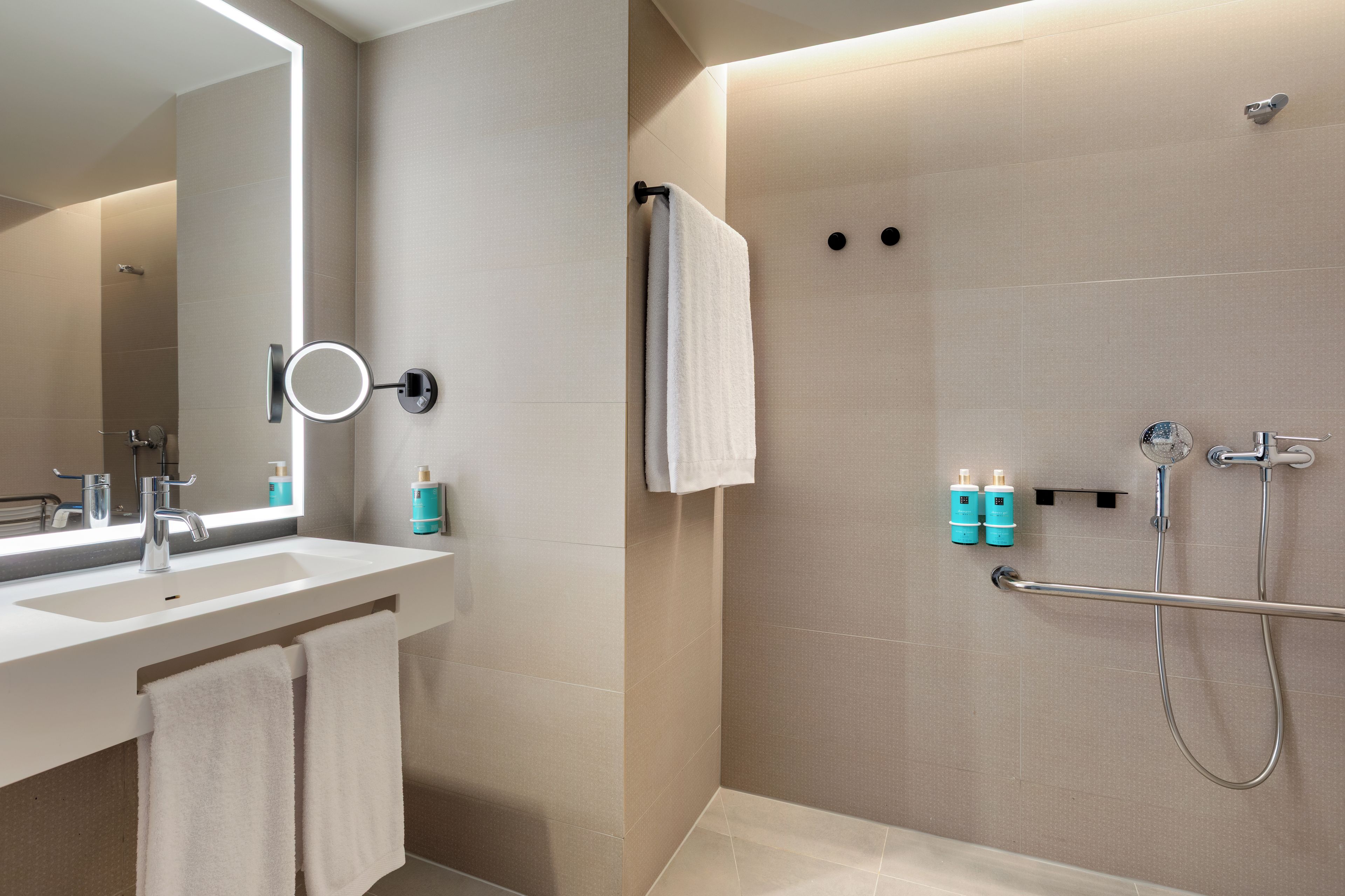 Un baño moderno con lavamanos, espejo, toallero y zona de ducha.