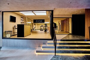 Un gimnasio moderno con un letrero, equipo de ejercicio y una escalera que lleva a un segundo piso.