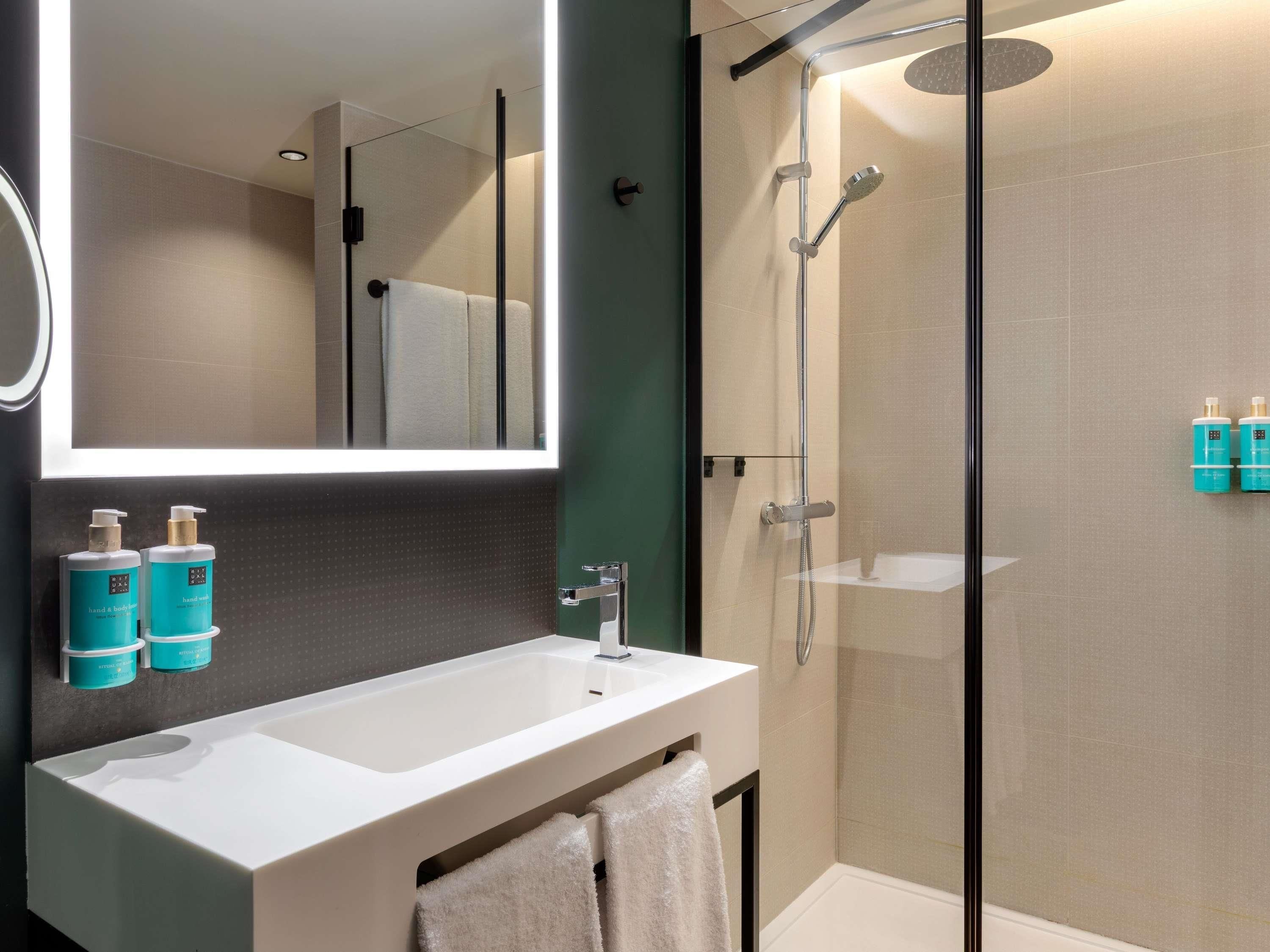 A modern bathroom with a glass-enclosed shower, a white sink, and two bottles of hand soap on the wall.