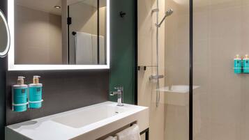 A modern bathroom with a glass-enclosed shower, a white sink, and two bottles of hand soap on the wall.