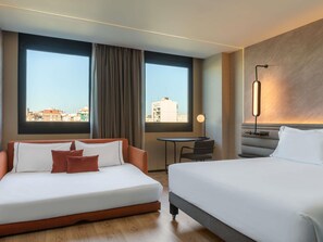 Habitación de hotel con cama, sofá, una mesita y vistas a la ciudad.