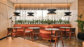 Un interior moderno con una zona de estar que incluye sofás naranja y sillas de madera, un ventanal con plantas e iluminación colgante.