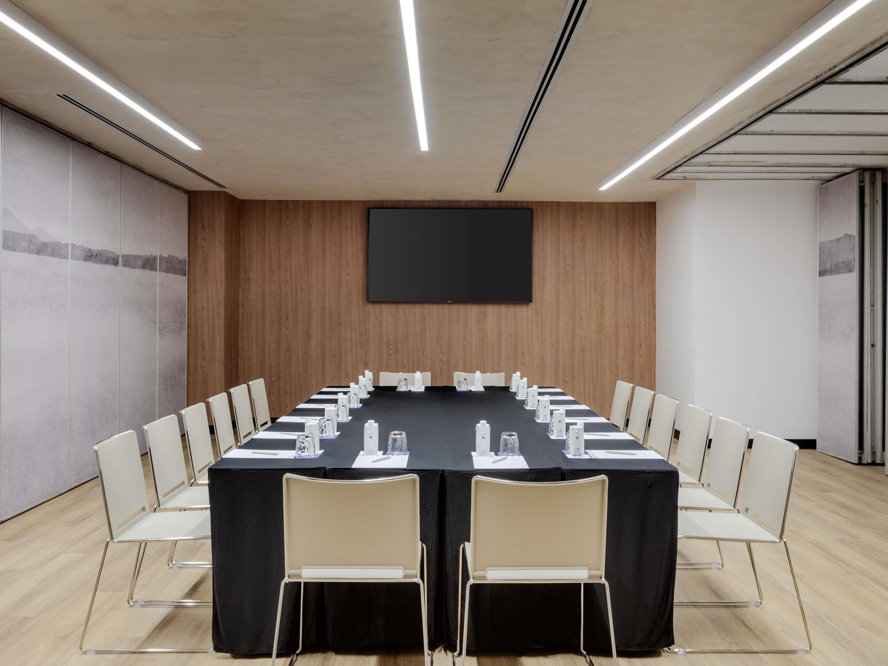 A conference room with a long table, chairs, a projector screen, and a wooden wall.