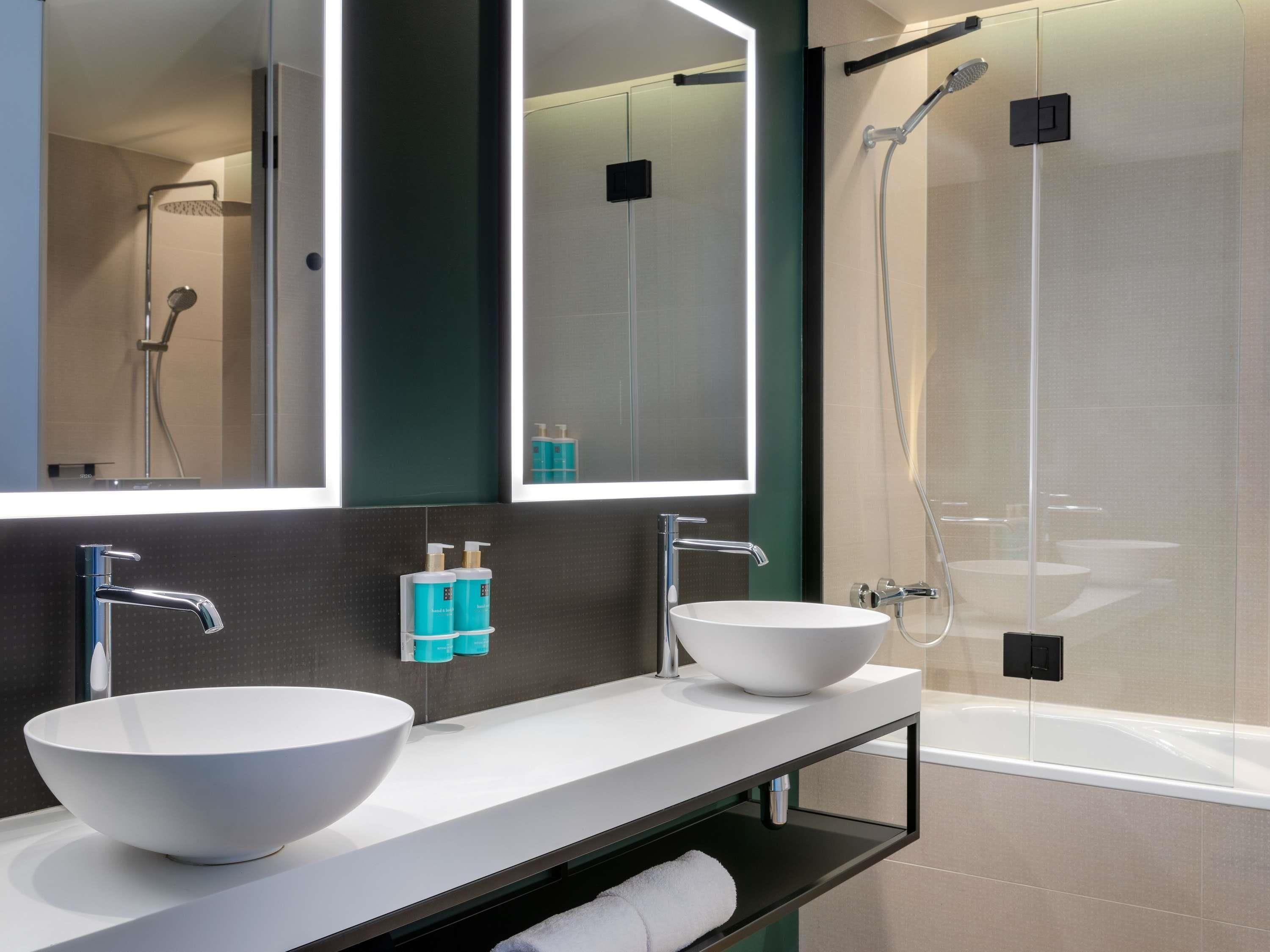 A modern bathroom with two sinks, a large mirror, and a glass-enclosed shower.