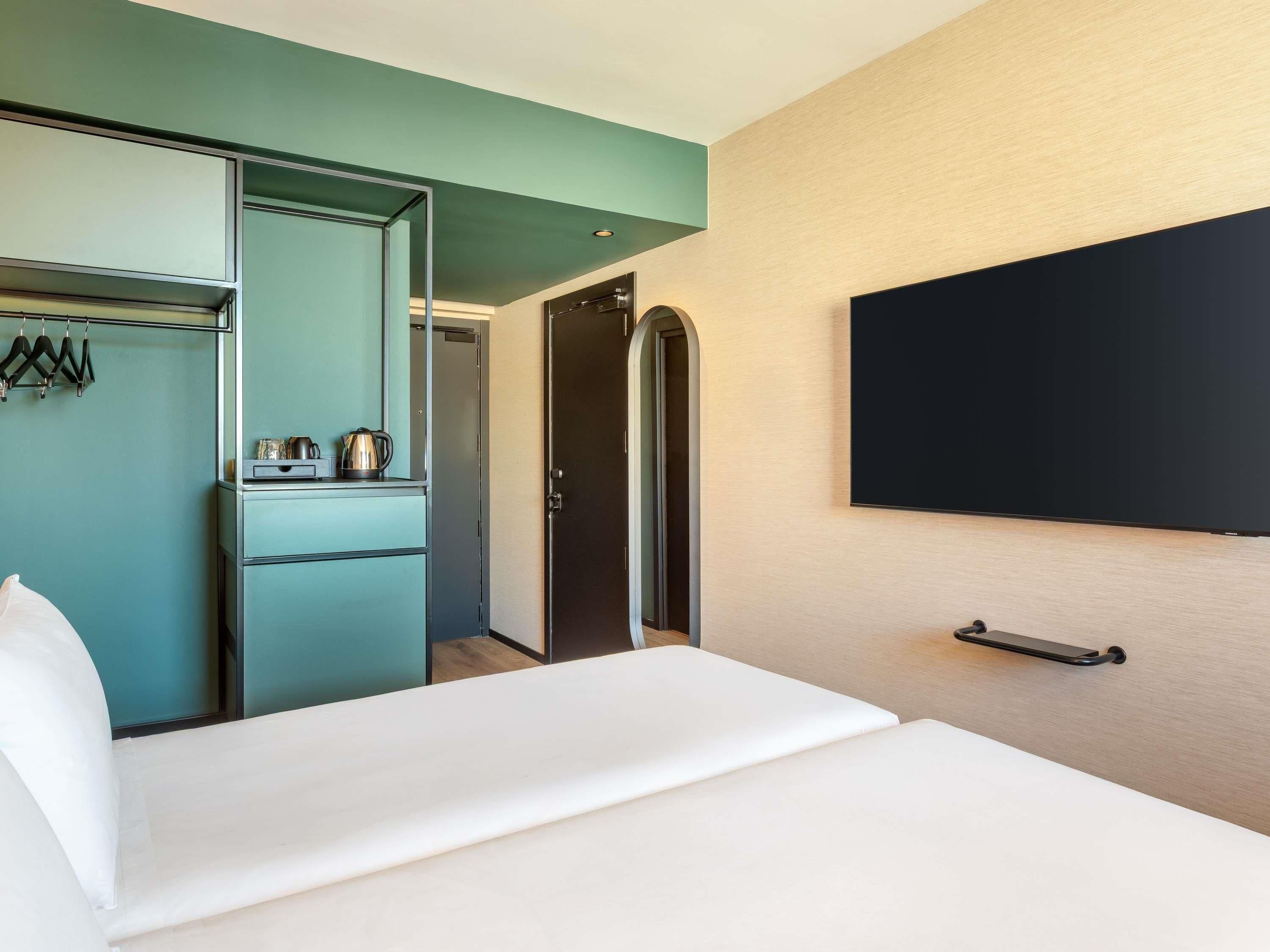 A hotel room with a bed, a wardrobe, a television, and a door leading to another room.