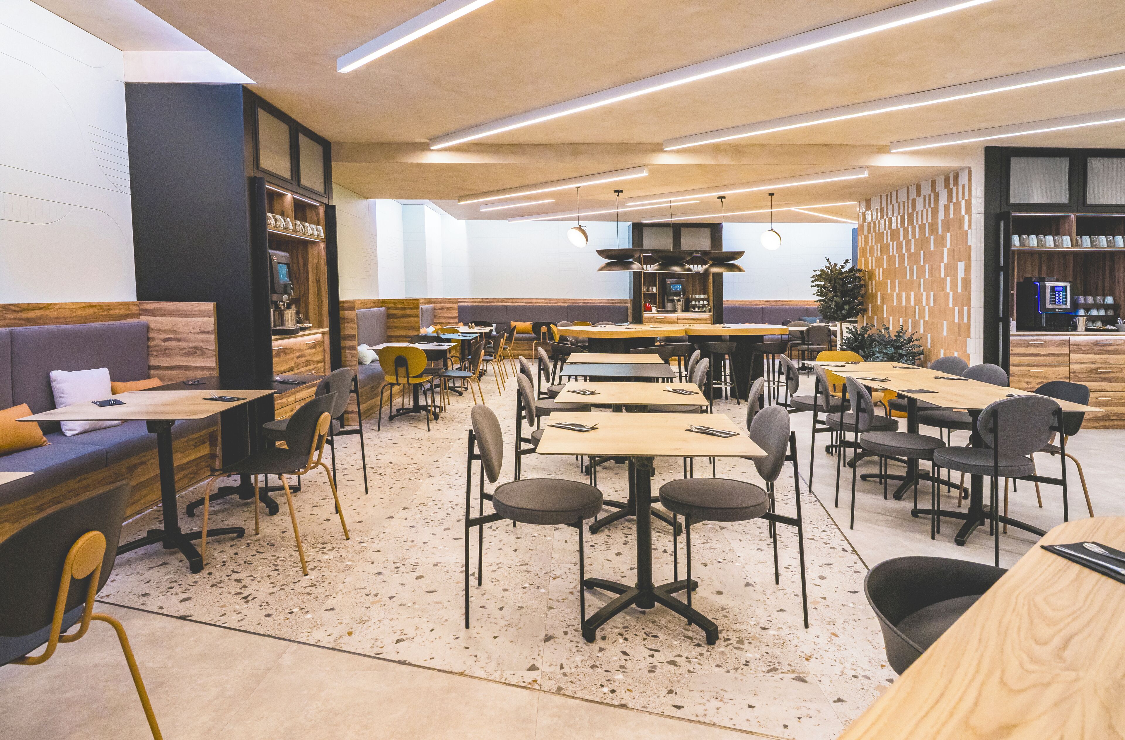Un restaurante moderno con varias zonas de comedor, incluyendo reservados y mesas con sillas.