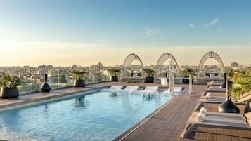 Una piscina en la azotea con sillones de descanso y plantas en macetas.