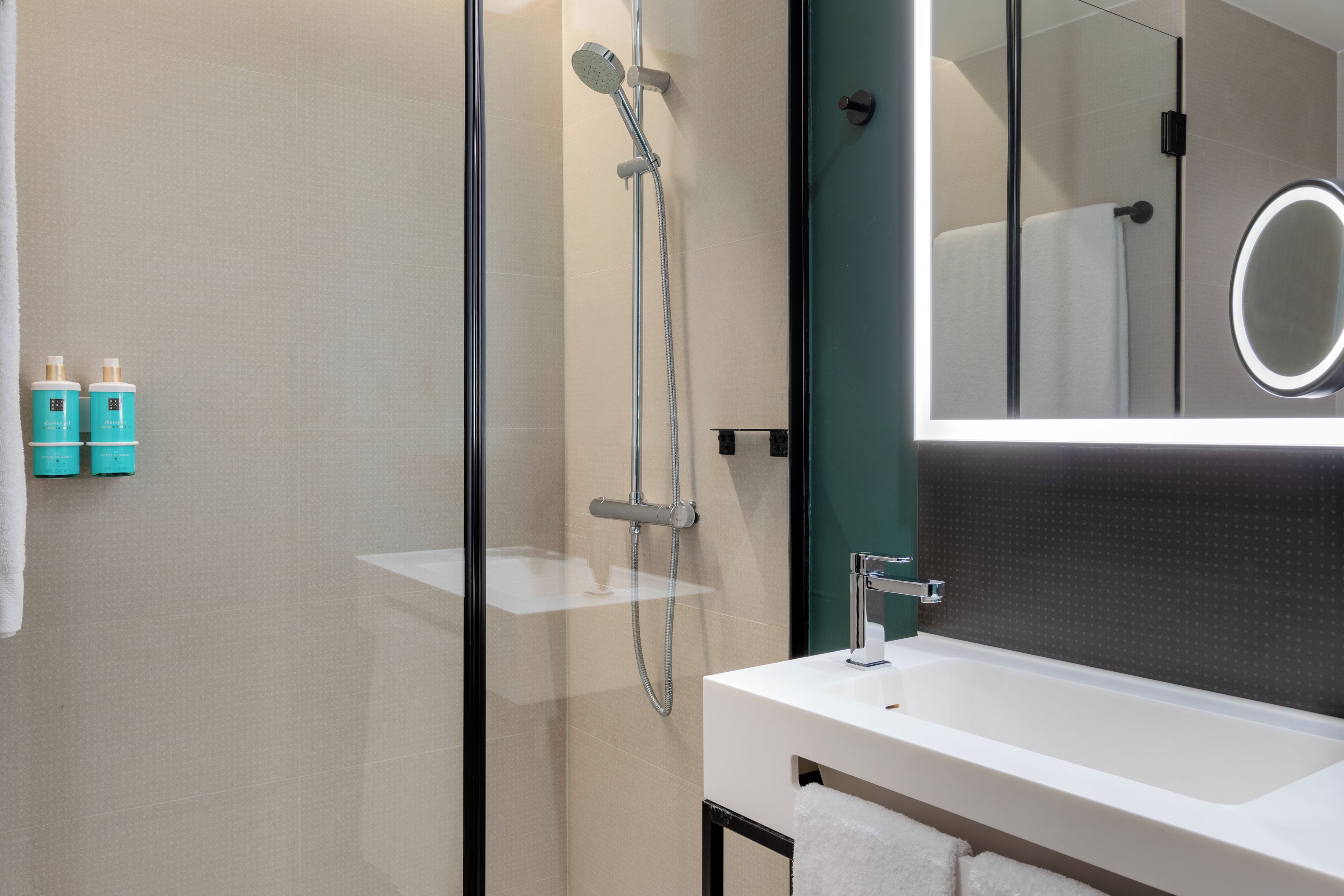 A modern bathroom with a glass-enclosed shower, a white sink, and a mirror with a circular light.