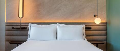A hotel room with a bed, two bedside tables, and a wall-mounted light fixture.