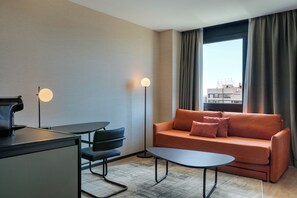 Una habitación de hotel moderna con un sofá, una mesita, una cafetera y una lámpara de pie.