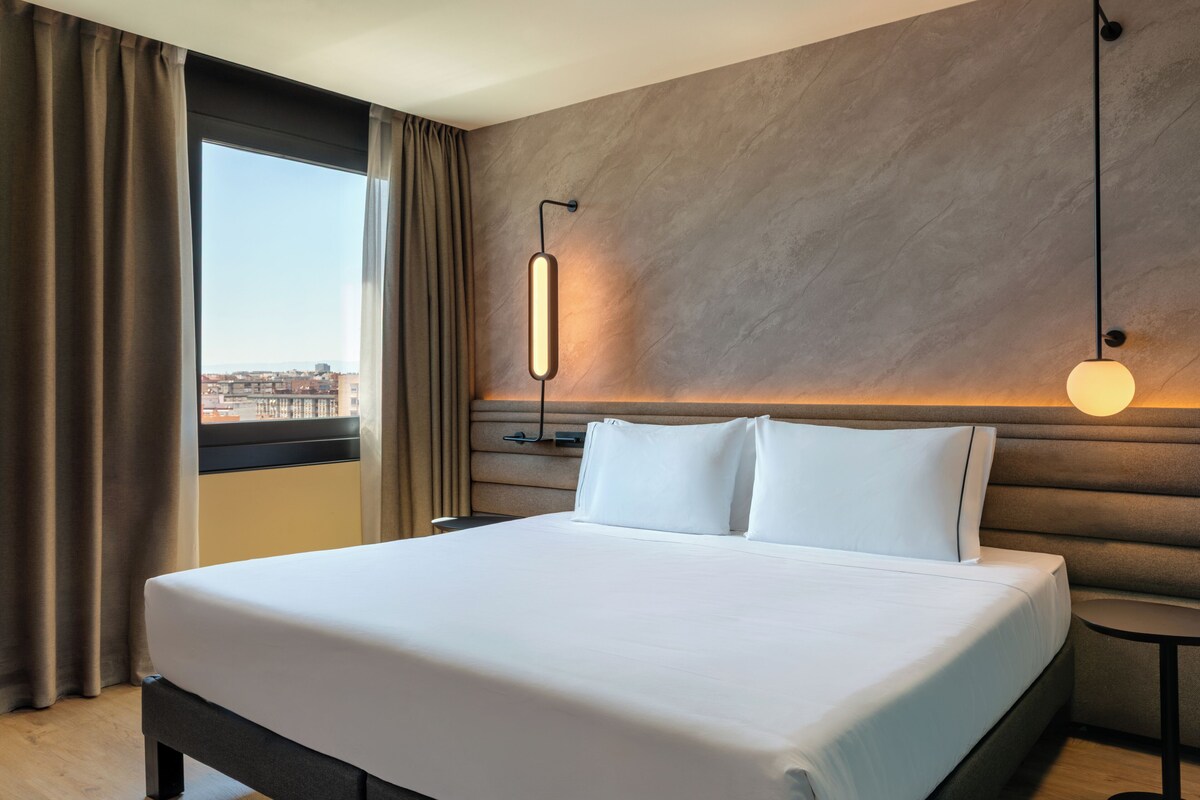 Habitación de hotel con una cama grande, vistas a la ciudad e iluminación moderna.