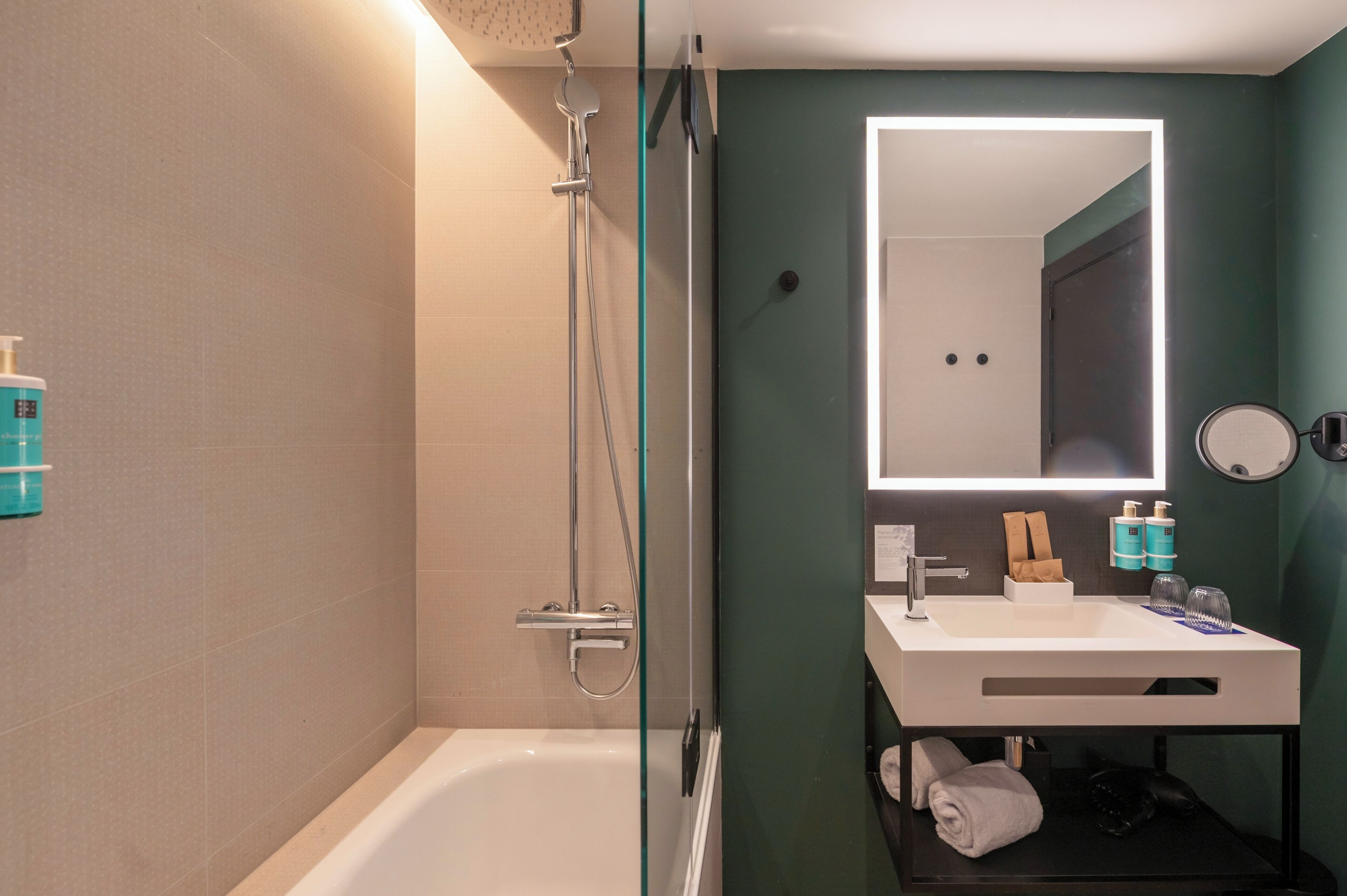 A modern bathroom with a glass-enclosed shower, a white sink with a mirror, and toiletries on the counter.