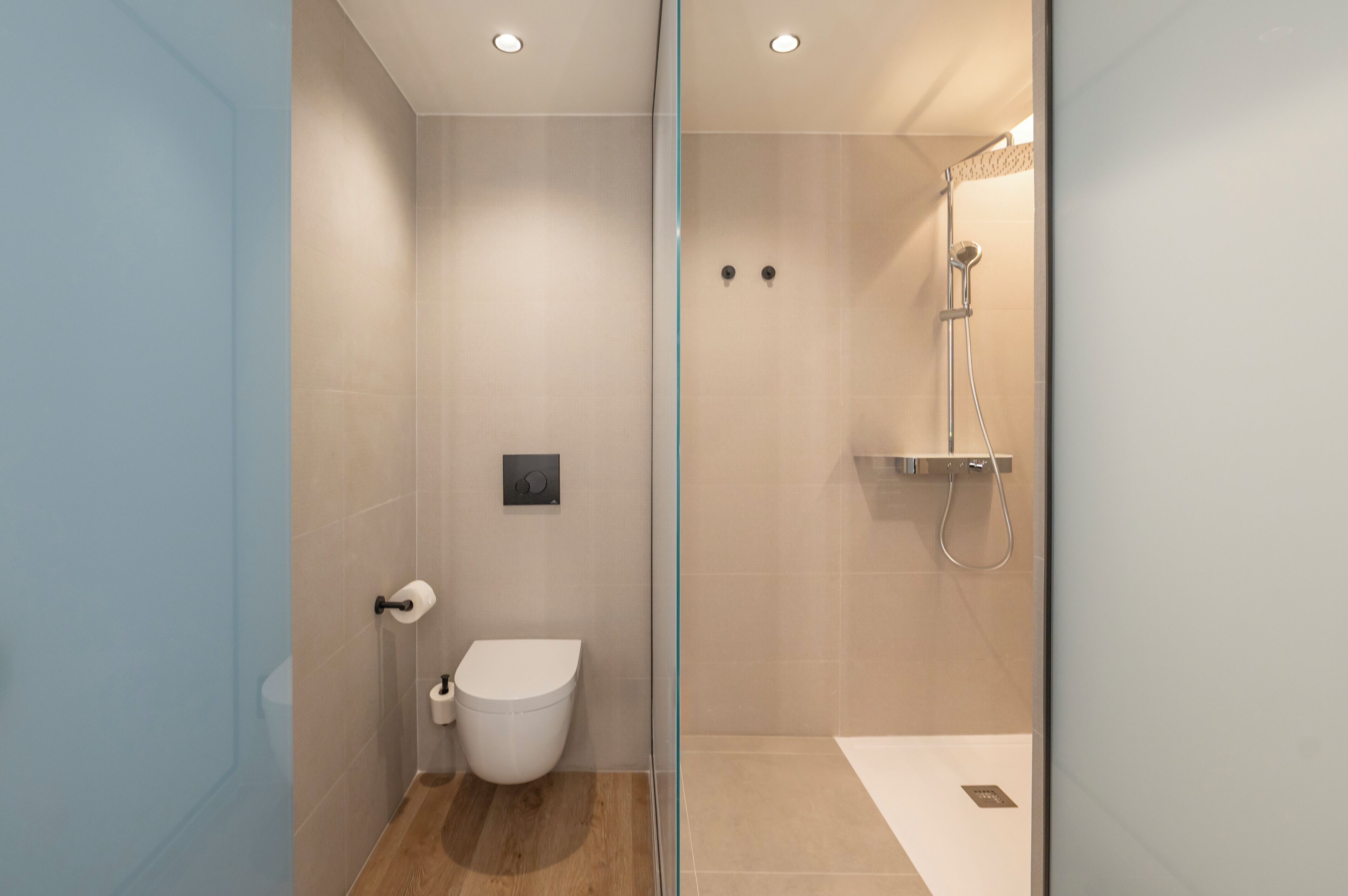 Et moderne badeværelse med en glasbrusekabine, toilet og et fastgjort skyl.