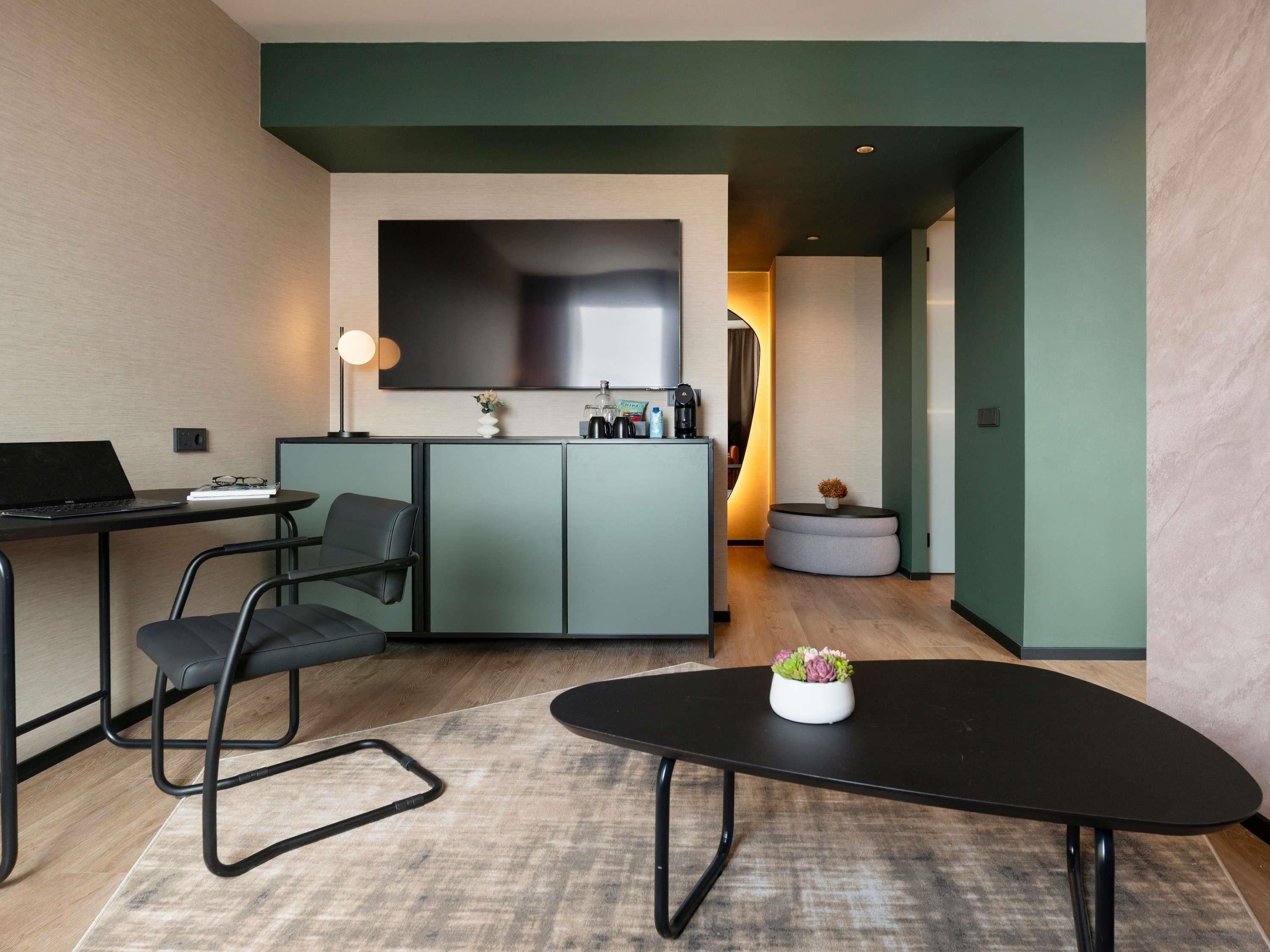 A modern, compact living space with a kitchenette, a flat-screen TV, a dining table, and a sofa.