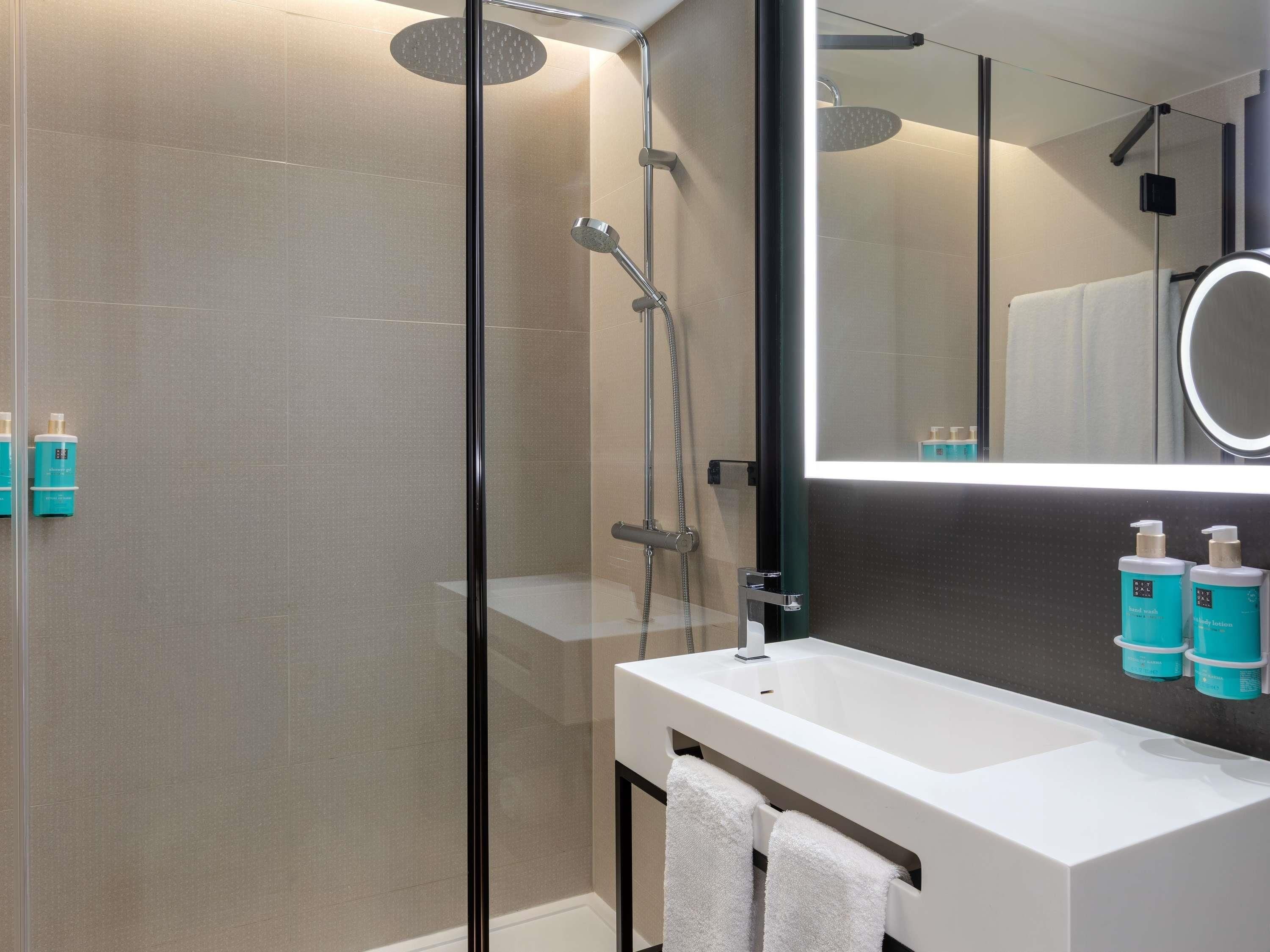 A modern bathroom with a glass-enclosed shower, a white sink, and a large mirror.