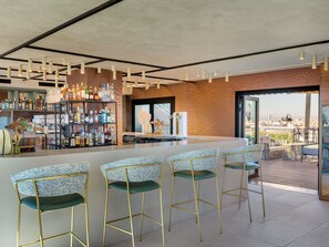 A modern bar area with a high ceiling, bar stools, and a variety of liquor bottles. - Novotel Valencia Lavant (Valencia)