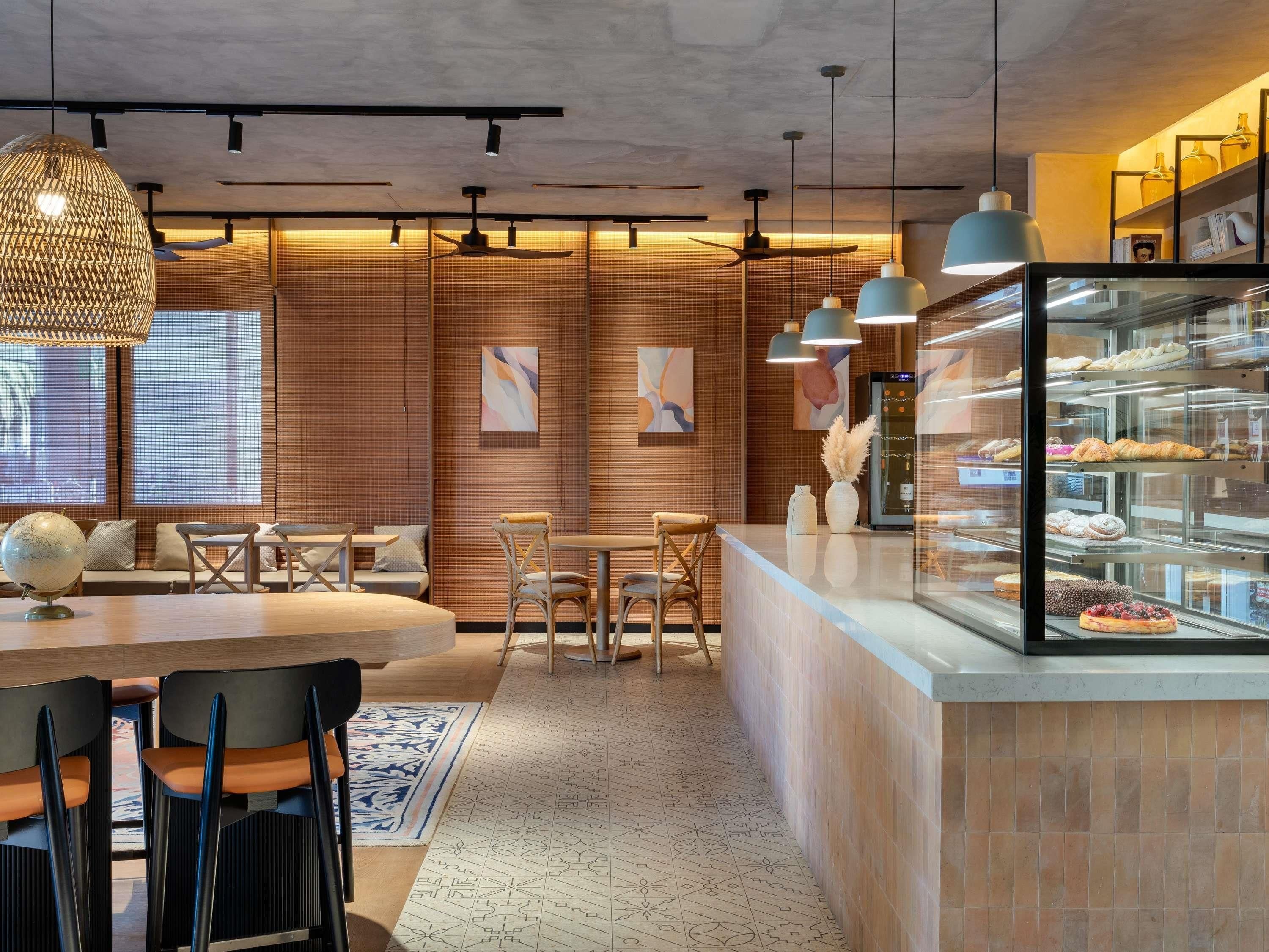 A modern cafe interior with a wooden wall, a glass display case with pastries, and a seating area with tables and chairs.
