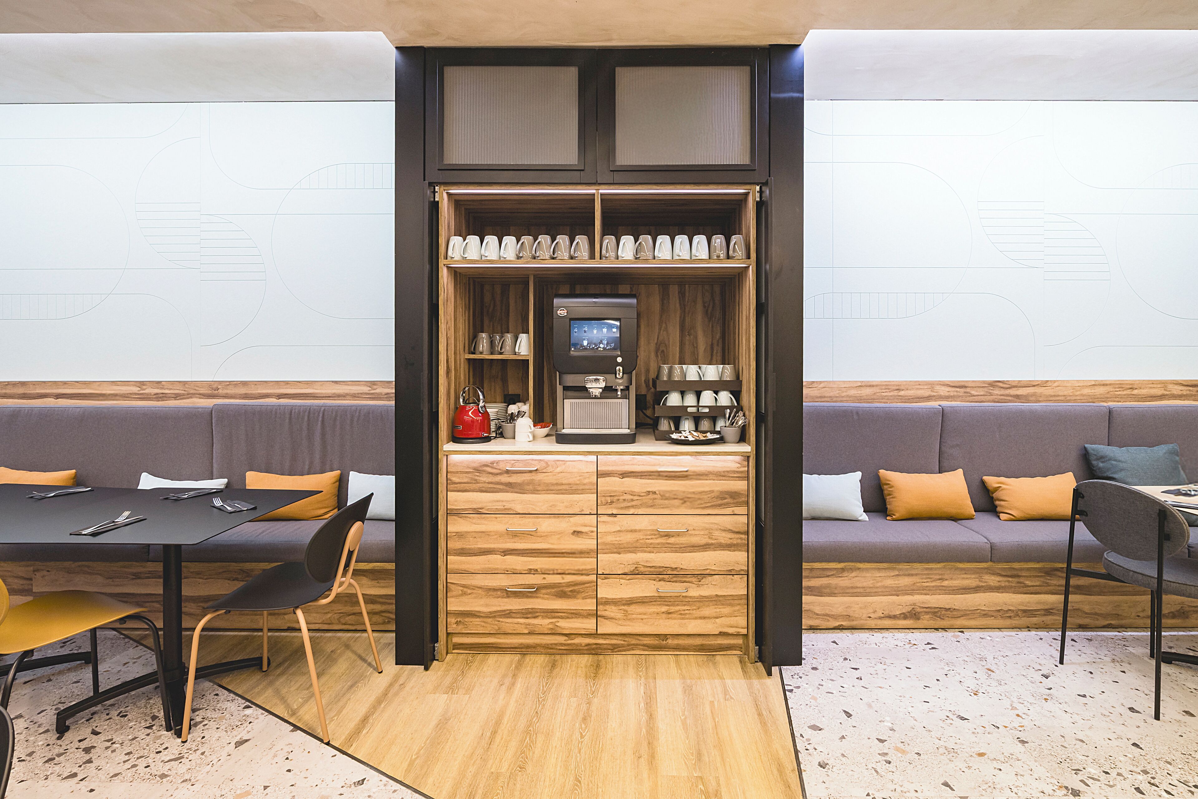 Un interior moderno con un mueble de madera que contiene vasos y una cafetera, un sofá y una mesa de comedor con sillas.