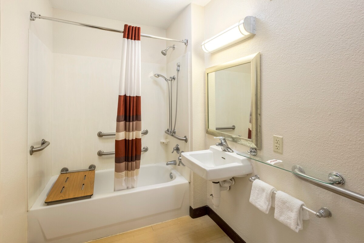 A modern bathroom with a bathtub, shower, glass-enclosed sink, and a mirror.