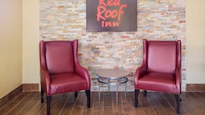 A Red Roof Inn with two leather chairs and a small table in a lobby with a stone wall backdrop. - Red Roof Inn Jacksonville - Orange Park (Jacksonville)