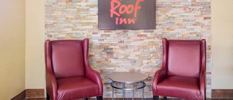 A Red Roof Inn with two leather chairs and a small table in a lobby with a stone wall backdrop.