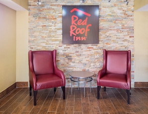 A Red Roof Inn with two leather chairs and a small table in a lobby with a stone wall backdrop. - Red Roof Inn Jacksonville - Orange Park (Jacksonville)