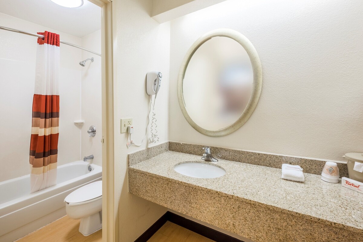 A bathroom with a bathtub, toilet, sink, and a round mirror.