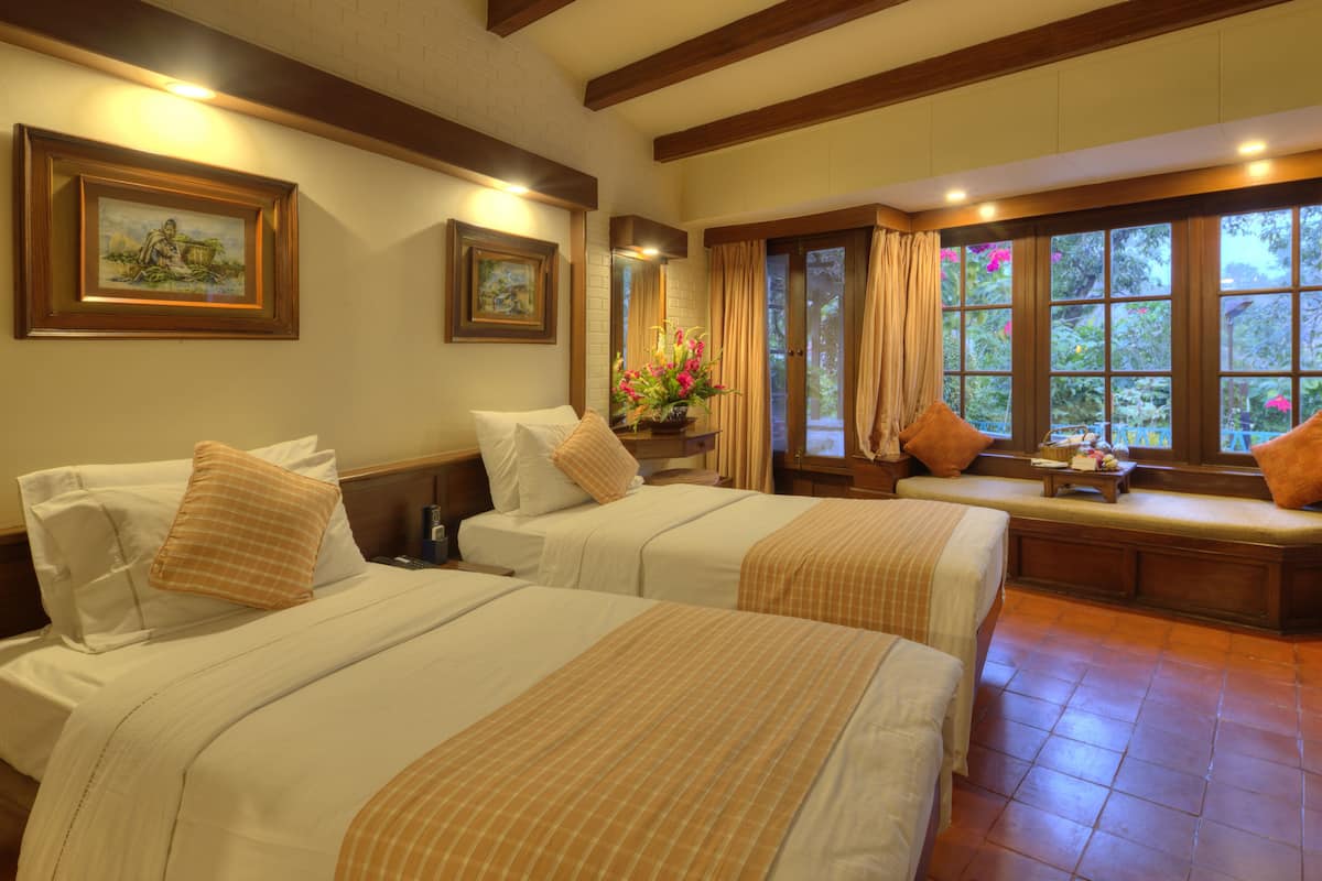 A hotel room with two beds, a bench, and a window with curtains.