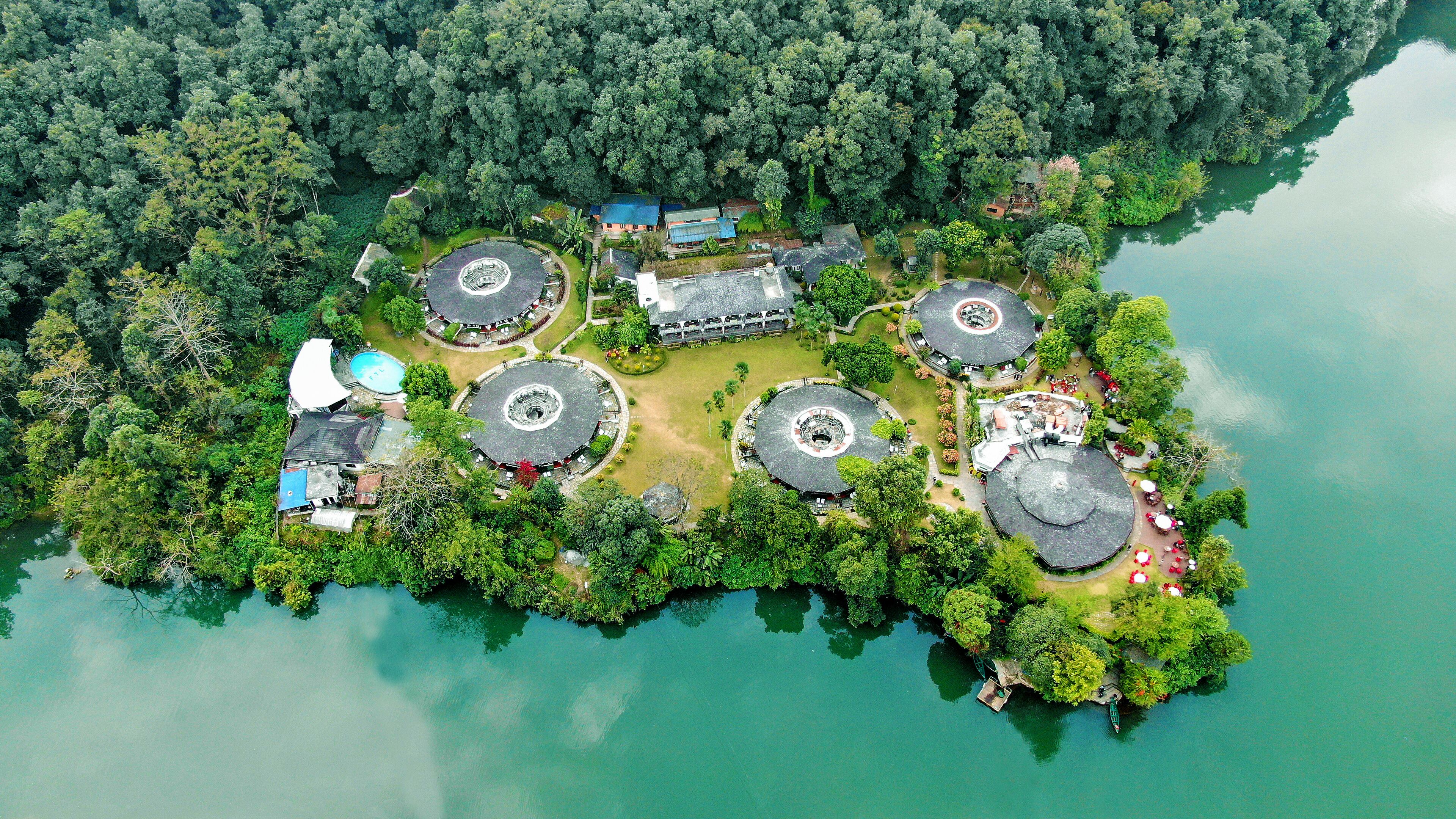 An aerial view of a resort island with multiple circular buildings, a swimming pool, and a dock.
