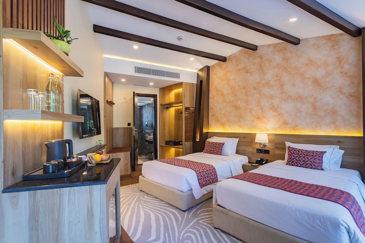 A hotel room with two beds, a kitchenette, a shower area, and a large mirror.