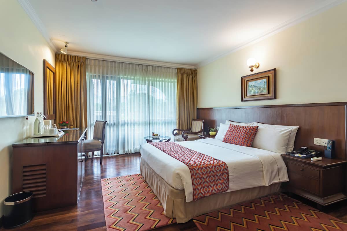 A hotel room with a large bed, a desk with a chair, a nightstand, and a window with curtains.