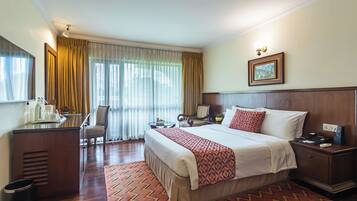 A hotel room with a large bed, a desk with a chair, a nightstand, and a window with curtains.