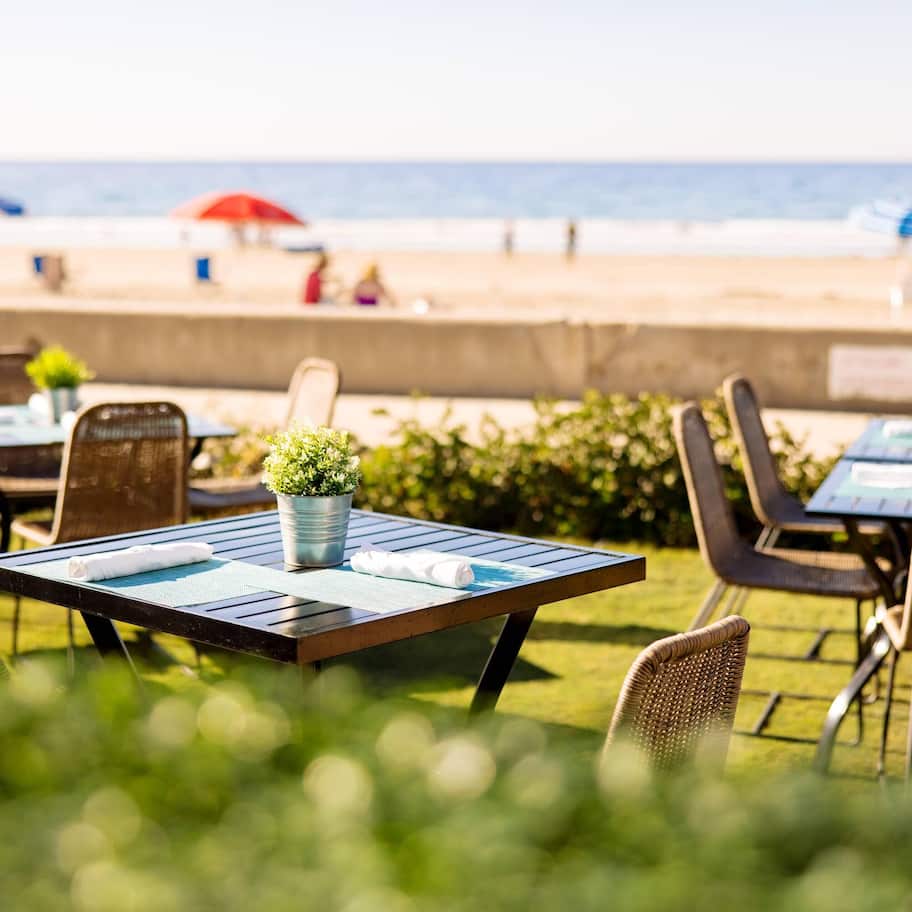 Outdoor tables and chairs with a view of the beach and ocean.