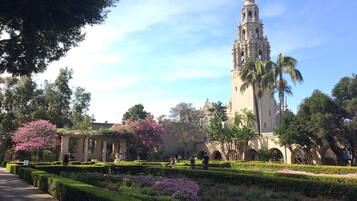 A historic building with a tall tower, surrounded by well-manicured gardens and palm trees.