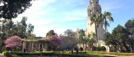 A historic building with a tall tower, surrounded by well-manicured gardens and palm trees.