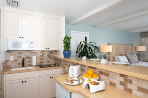 A modern kitchen with white cabinets, a microwave, a toaster, and a breakfast setup including bread, butter, and oranges.