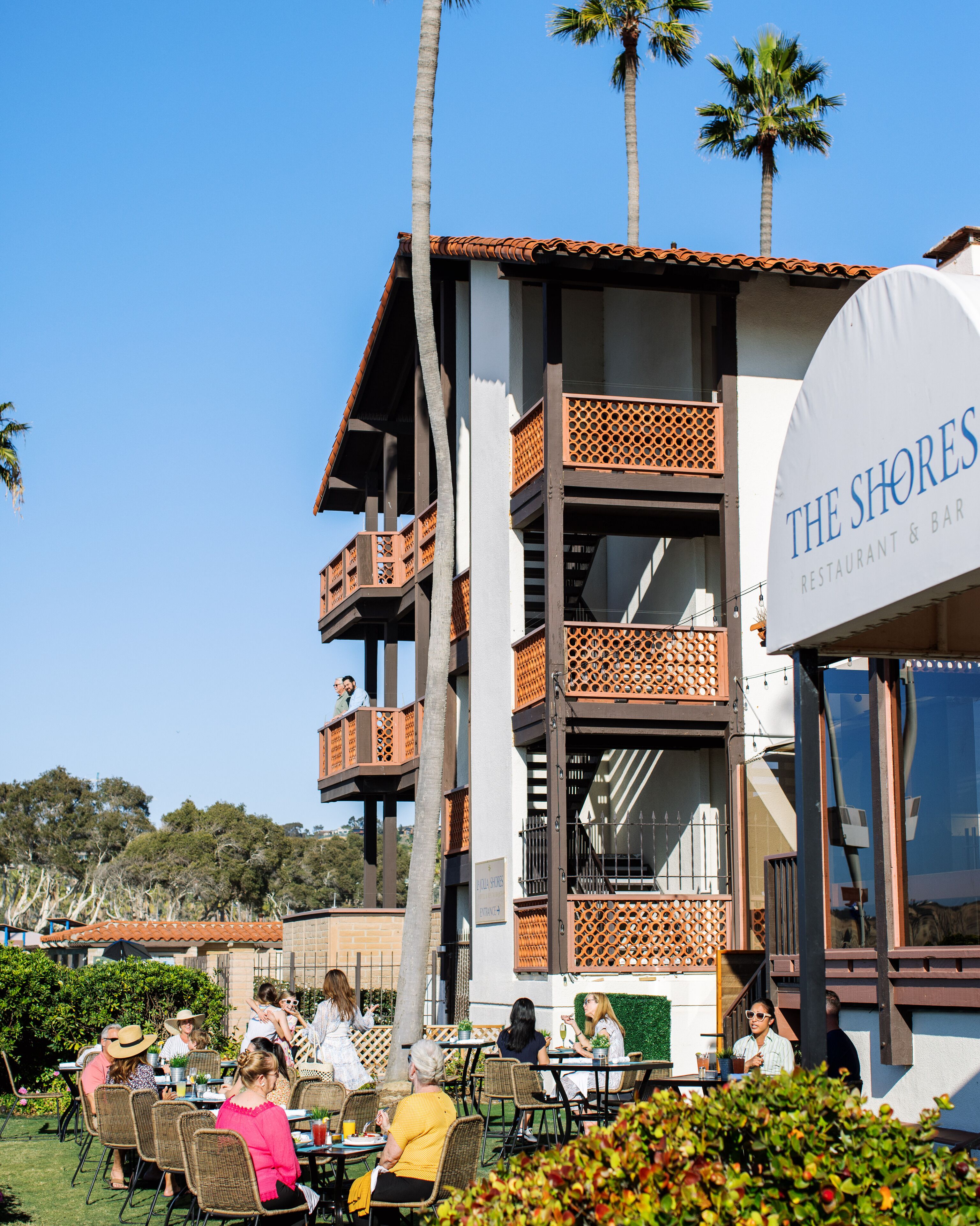 A restaurant with outdoor seating, a sign reading "The Shores Restaurant & Bar", and palm trees in the background.