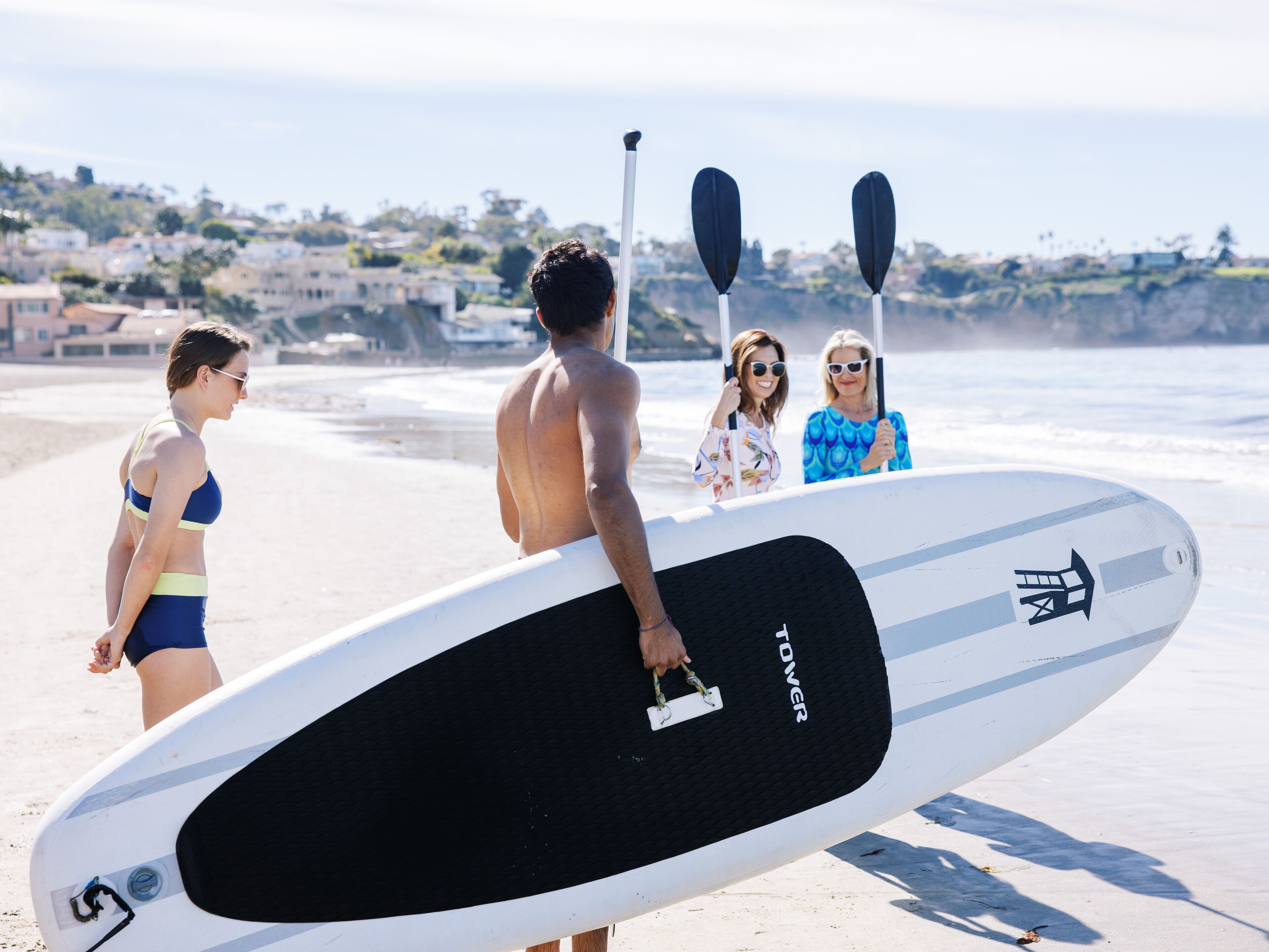 A beach scene with a surfboard, a paddleboard, and a person holding a paddle.