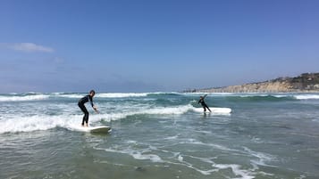 Deux surfeurs sur une plage, avec des vagues, une jetée en arrière-plan et un paysage vallonné.