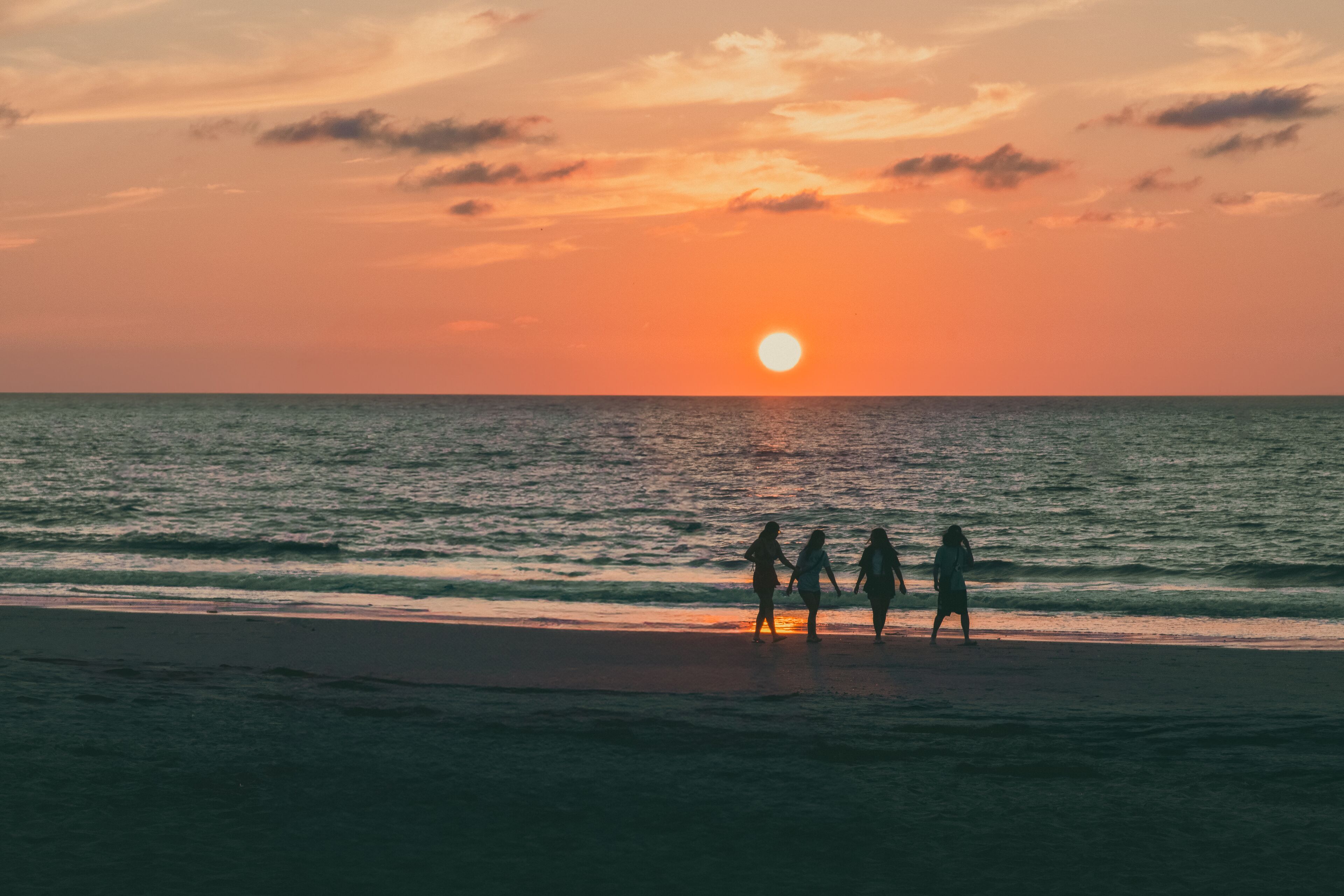 A sunset over the ocean with silhouettes of people on the beach.