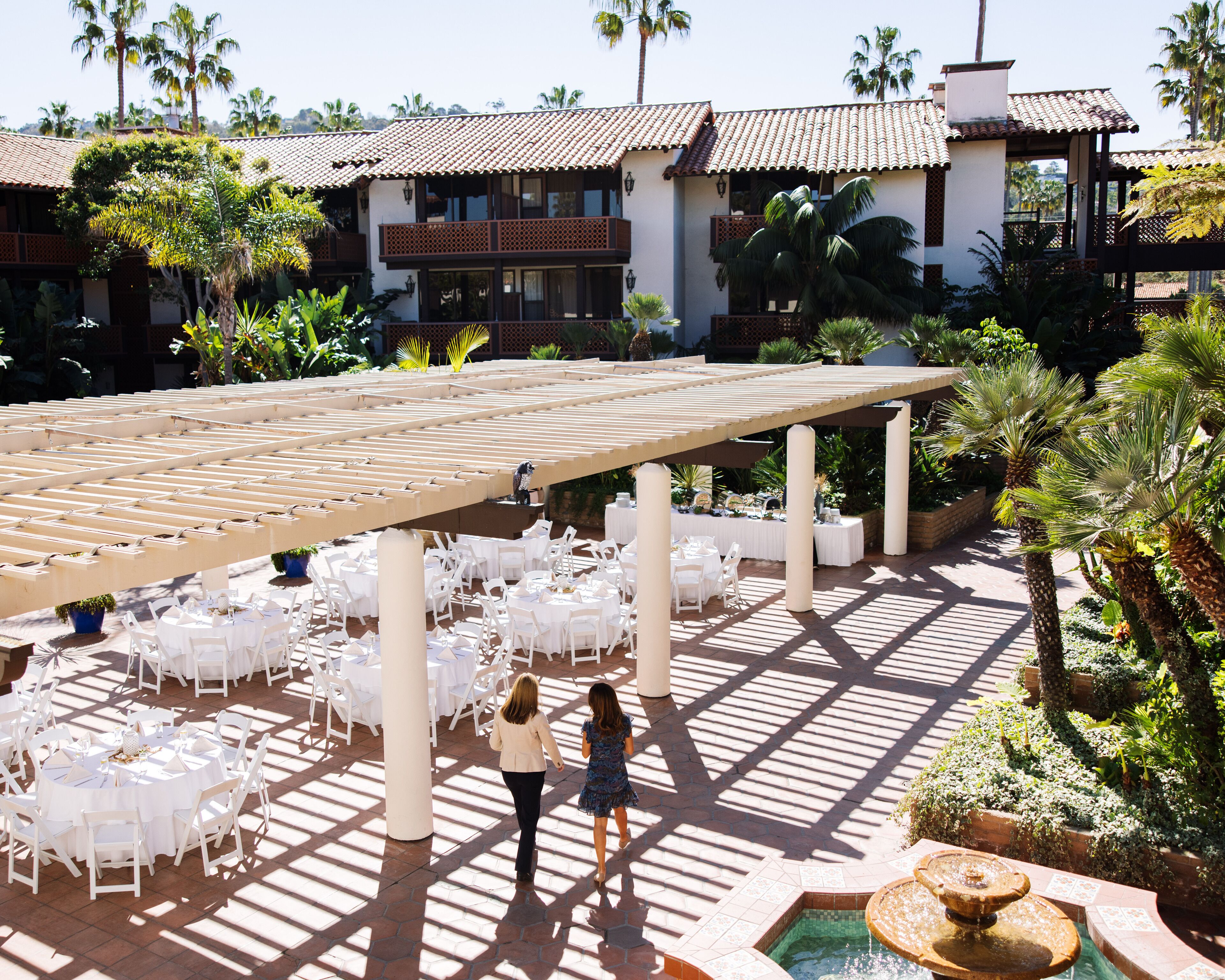 A covered outdoor dining area with white tables and chairs, a pergola, and a fountain.