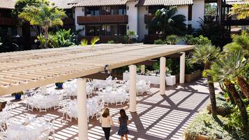 A covered outdoor dining area with white tables and chairs, a pergola, and a fountain.