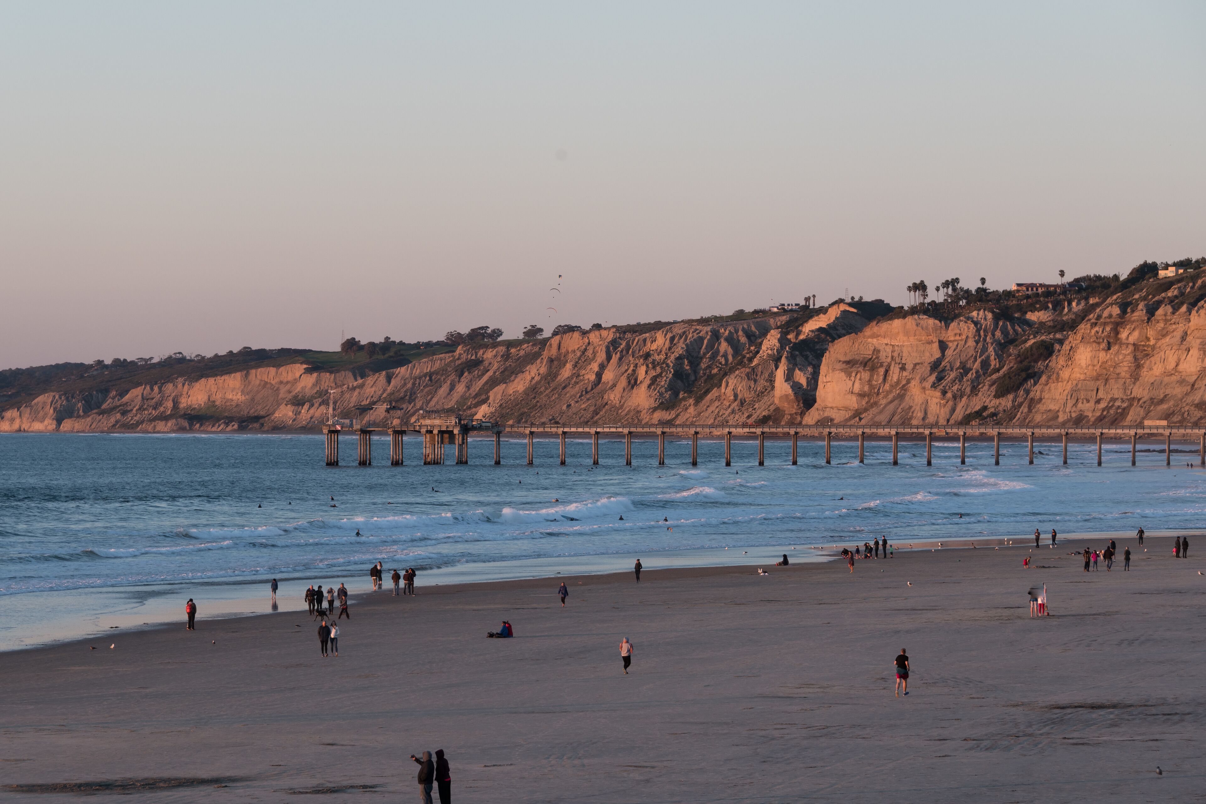 A beach with people, a pier, and cliffs in the background.